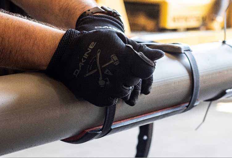an image of someone with gloves hand tightening the smartbands to secure the smartpad system to the pipe