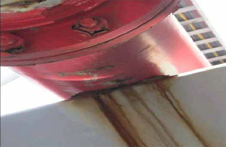 an image of a red coated pipe resting on a steel pipe support in an industrial pipe rack that has corrosion build up at the point of where the pipe is resting on the support